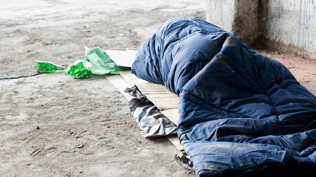 homeless person sleeping in sleeping bag on cardboard 
